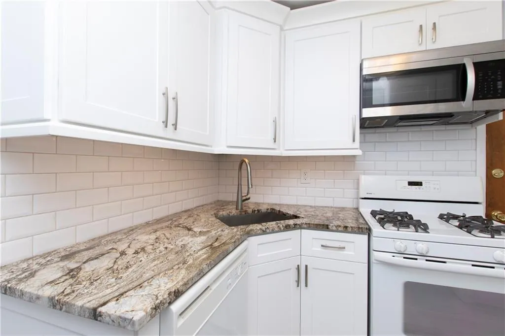 Kitchen featuring white appliances, tasteful backsplash, white cabinets, and light stone countertops