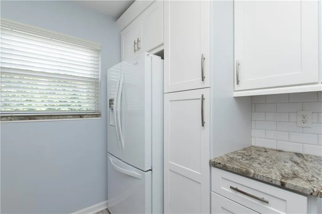Kitchen with white cabinets, white refrigerator with ice dispenser, light stone countertops, and backsplash