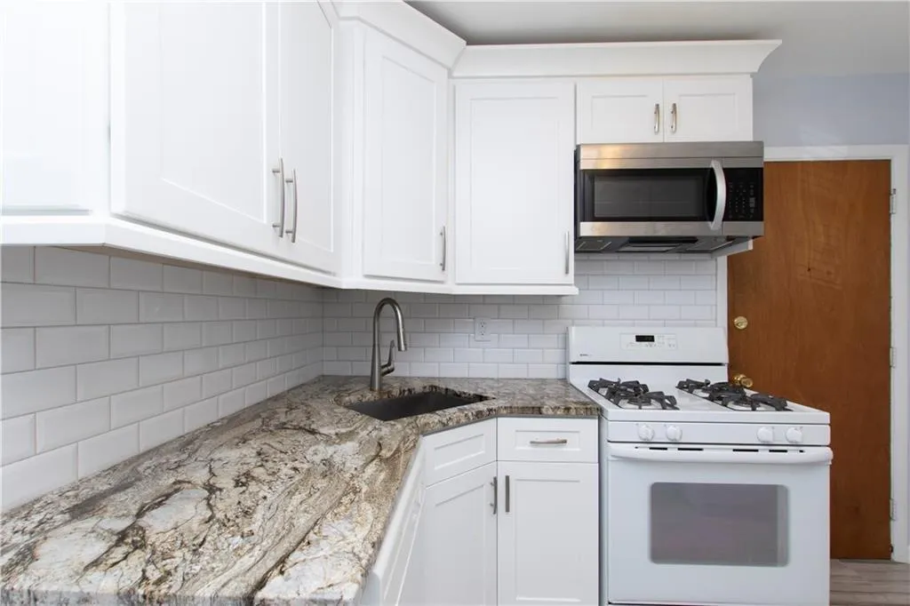 Kitchen with tasteful backsplash, white range with gas stovetop, white cabinetry, and stainless steel microwave