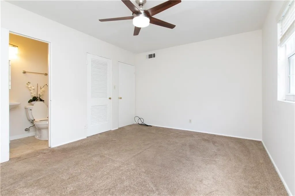 Unfurnished bedroom with light colored carpet, ceiling fan, connected bathroom, and a closet