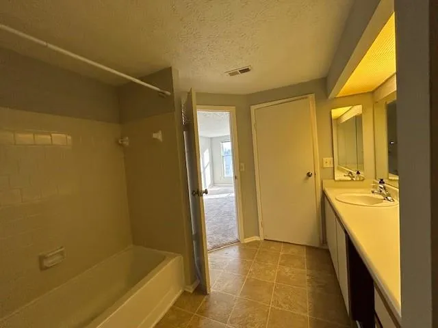 Bathroom with a textured ceiling, vanity, and washtub / shower combination