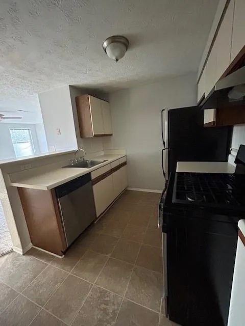 Kitchen with stove, sink, dishwasher, a textured ceiling, and white cabinets