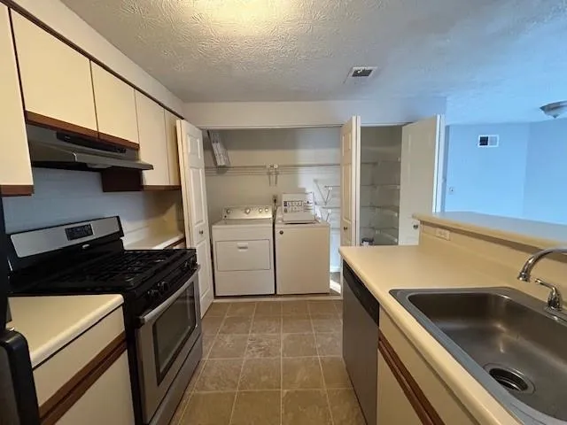 Kitchen featuring stainless steel appliances, a textured ceiling, washer and clothes dryer, white cabinets, and sink
