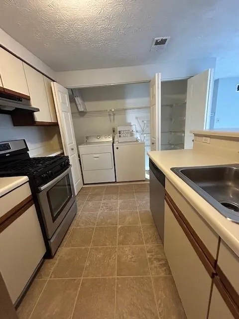 Kitchen featuring independent washer and dryer, stove, white cabinetry, dishwasher, and ventilation hood