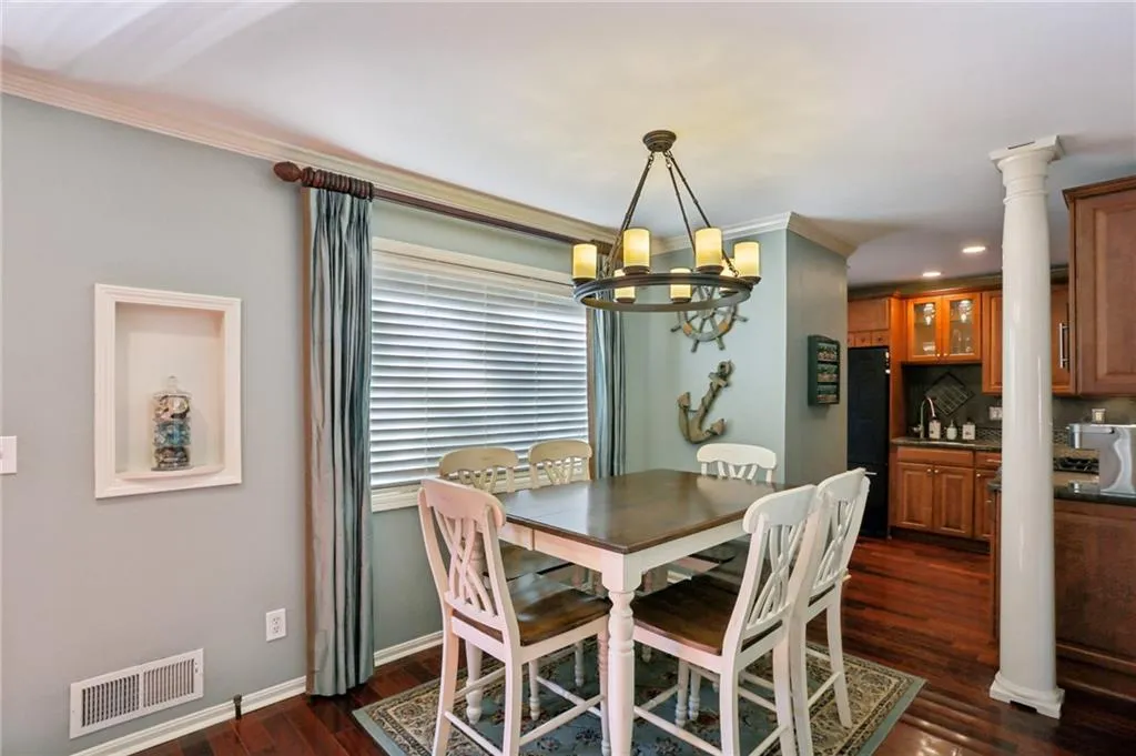 Dining area with dark wood-type flooring, ornate columns, a notable chandelier, and ornamental molding