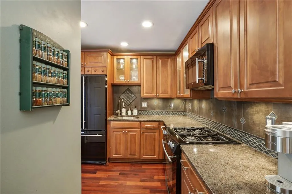 Kitchen featuring backsplash, black appliances, light stone counters, sink, and dark hardwood / wood-style floors