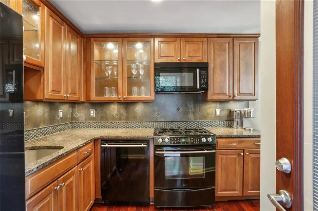 Kitchen featuring black appliances, tasteful backsplash, dark hardwood / wood-style floors, and stone countertops