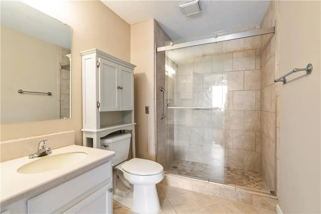 Bathroom featuring toilet, vanity, a textured ceiling, and a shower stall