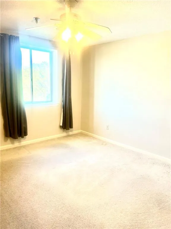 Carpeted empty room featuring baseboards, a textured ceiling, and a ceiling fan