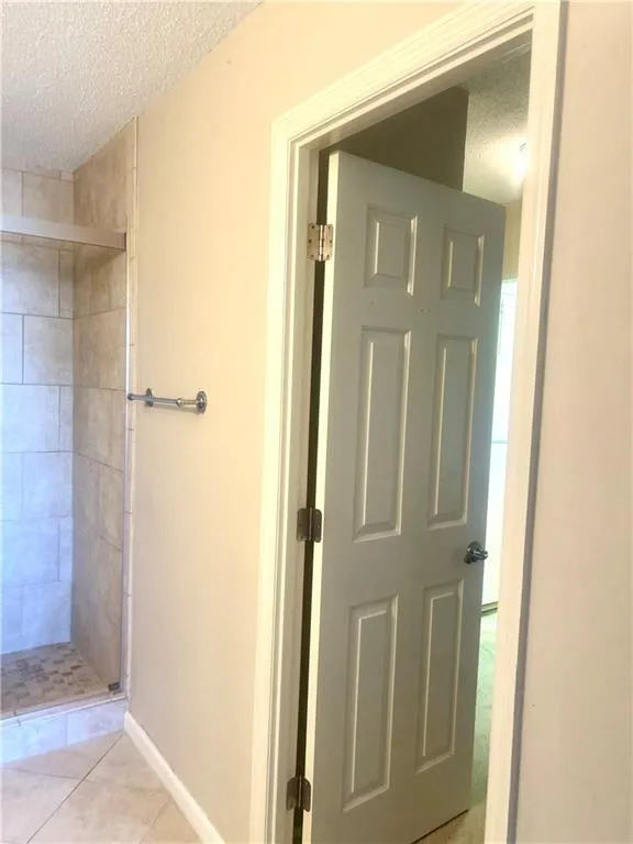Full bath featuring tile patterned floors, baseboards, easy walk-in tiled shower, and a textured ceiling
