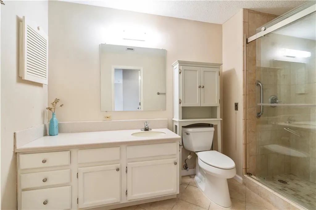 Bathroom with toilet, a textured ceiling, vanity, easy walk-in shower with glass door, and tile patterned flooring