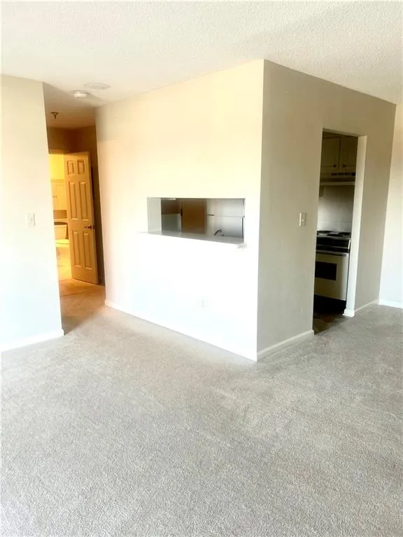 Unfurnished living room with baseboards, a textured ceiling, and carpet