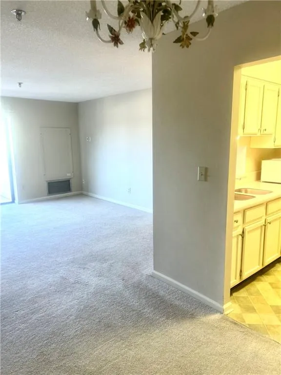 Unfurnished living room with baseboards, a textured ceiling, a sink, and light colored carpet