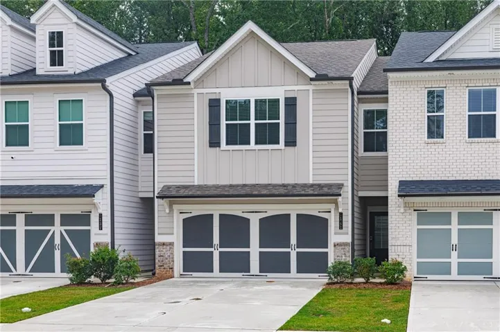Multi-story residence featuring light gray siding, dark gray shutters, and a two-car garage with arched design elements