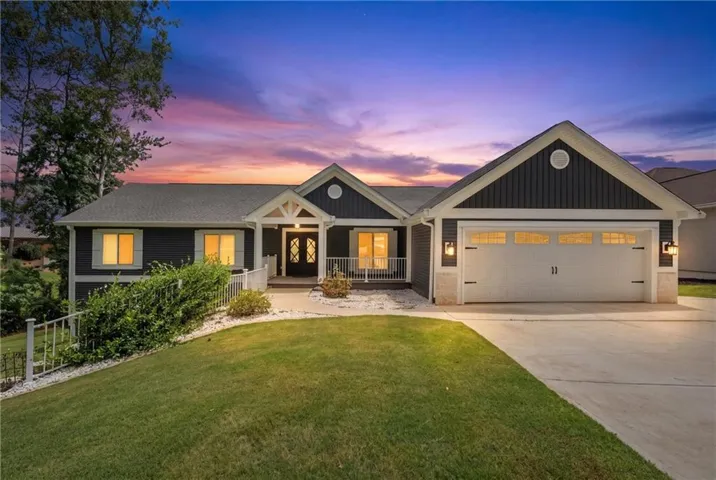 Modern ranch home featuring dark horizontal siding, white trim accents, a two-car garage with carriage-style doors, a gabled entry porch, and a concrete driveway