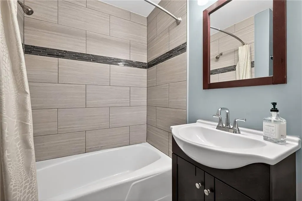 Main Floor Secondary Bath | Neutral Tile with Accent Band | Soaking Tub | Vanity Storage