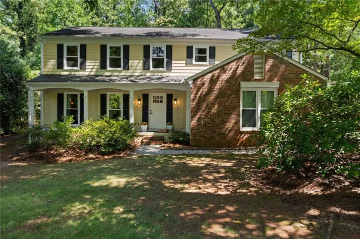 Two-story exterior with a covered porch, brick facade accents, and mature trees