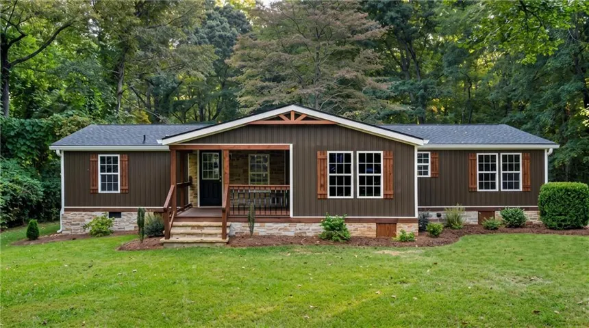 Exterior featuring dark vertical siding, white-framed windows with decorative wood shutters, a covered front porch with wood railings, and a stone-clad foundation