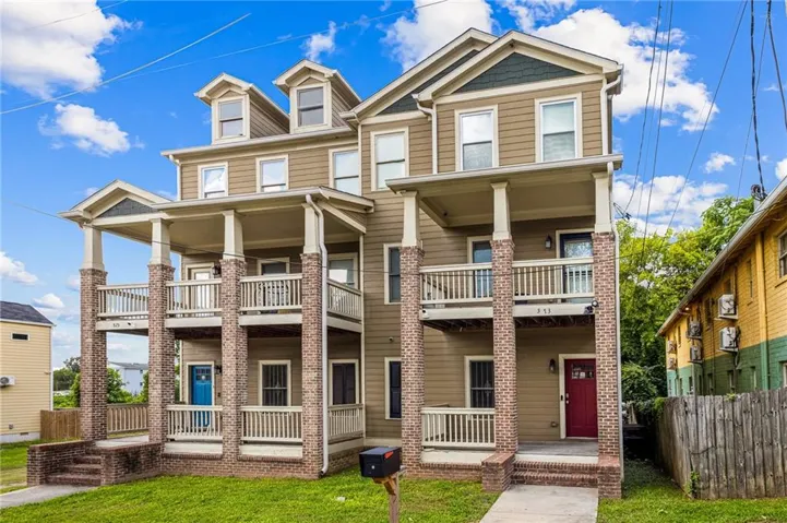 Three-story multi-unit dwelling with dormer windows, individual balconies, brick columns, and a covered porch