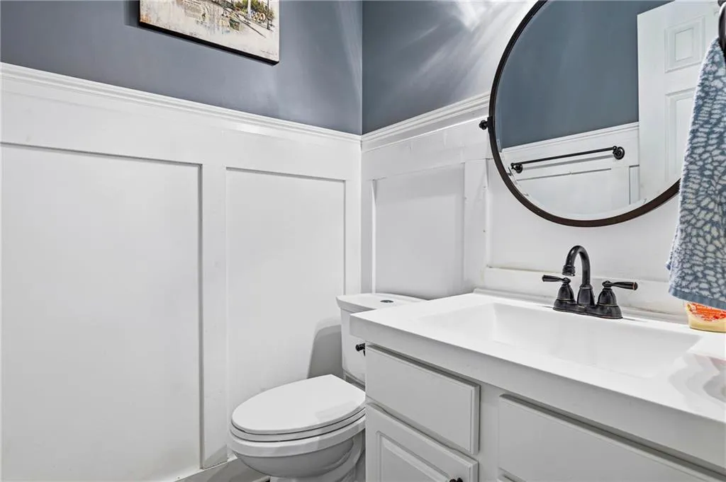 Board and batten wainscoting, integrated sink vanity with cabinet storage, round wall-mounted mirror, and dark bronze-finish fixtures