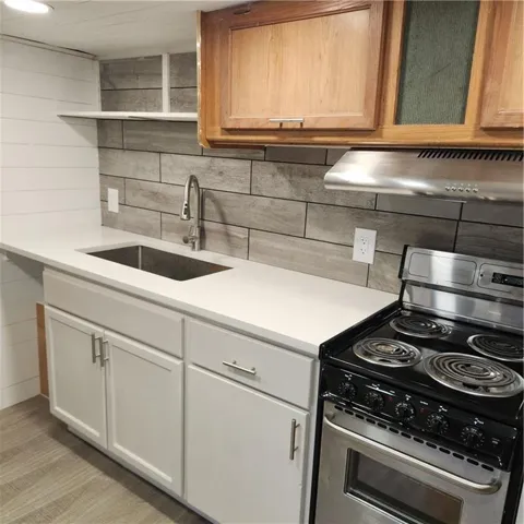 Kitchen with range, light countertops, open shelves, ventilation hood, and tasteful backsplash