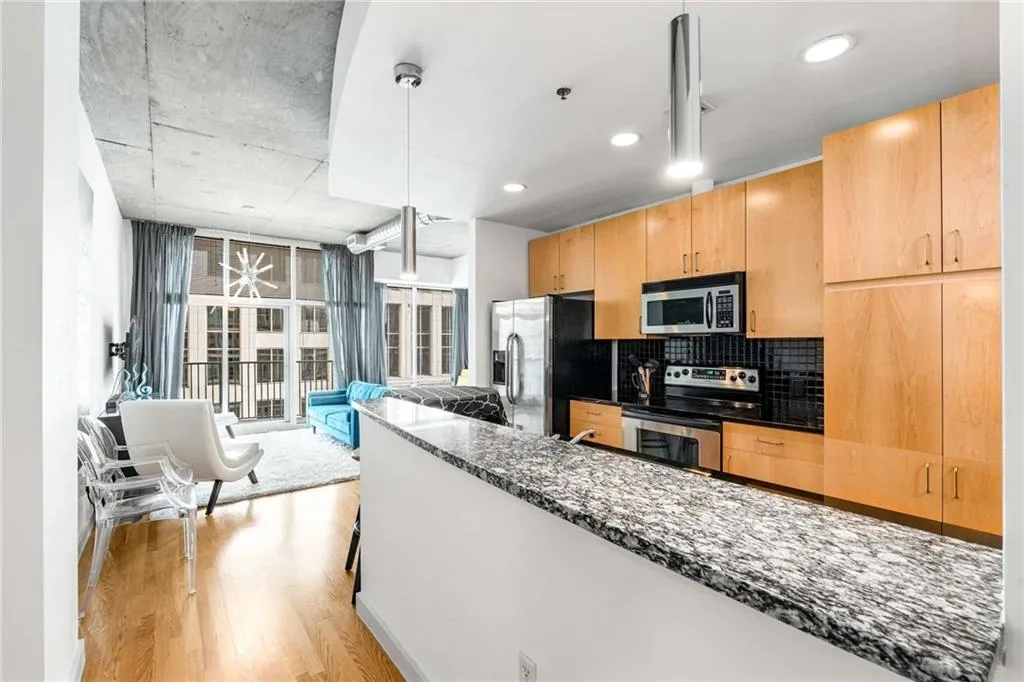 Kitchen with dark stone countertops, decorative backsplash, appliances with stainless steel finishes, light wood-style floors, and a wall of windows