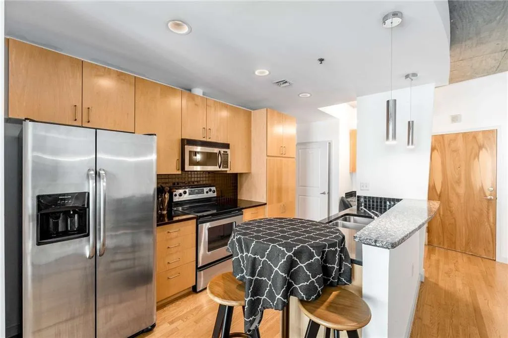 Kitchen featuring appliances with stainless steel finishes, pendant lighting, light wood finished floors, decorative backsplash, and a peninsula