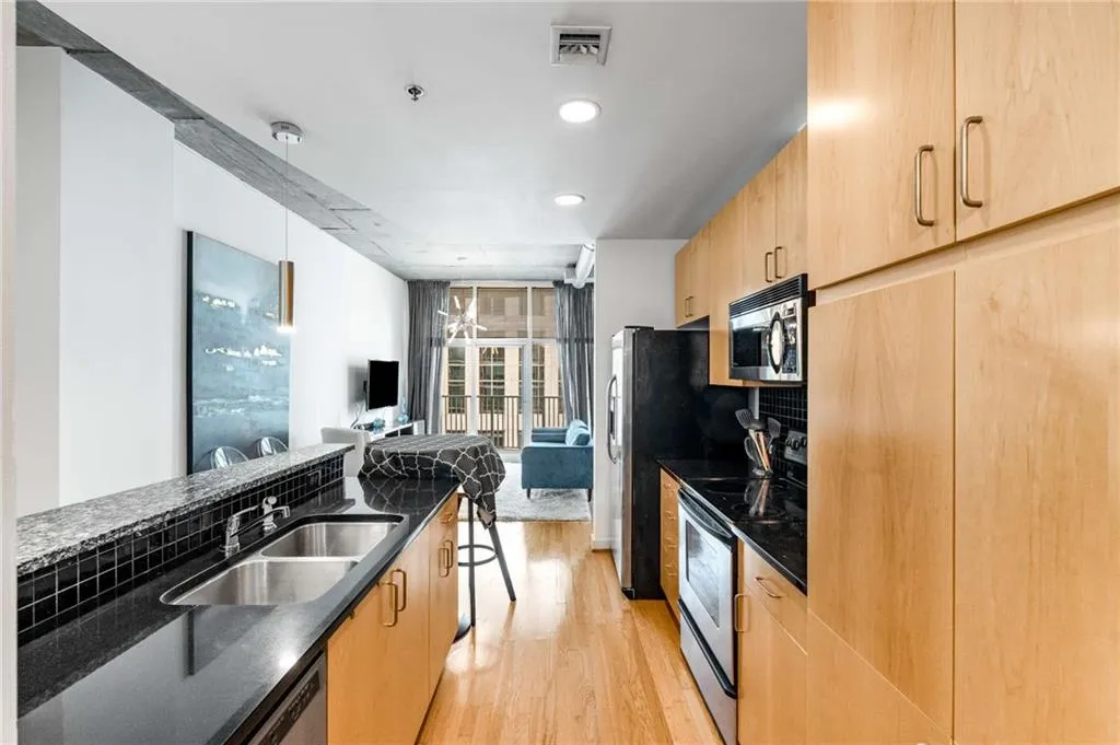 Kitchen with modern cabinets, dark stone countertops, stainless steel appliances, light brown cabinetry, and recessed lighting
