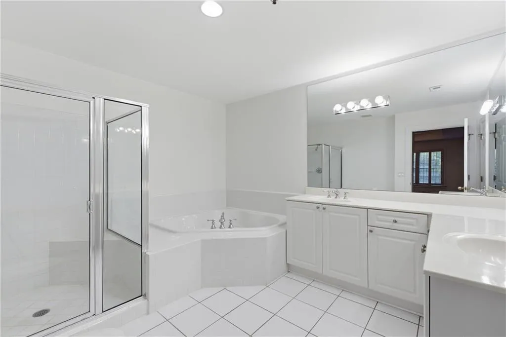 Bathroom featuring a glass-enclosed shower, corner soaking tub, dual vanity with white cabinetry, large wall-mounted mirror, and tile flooring