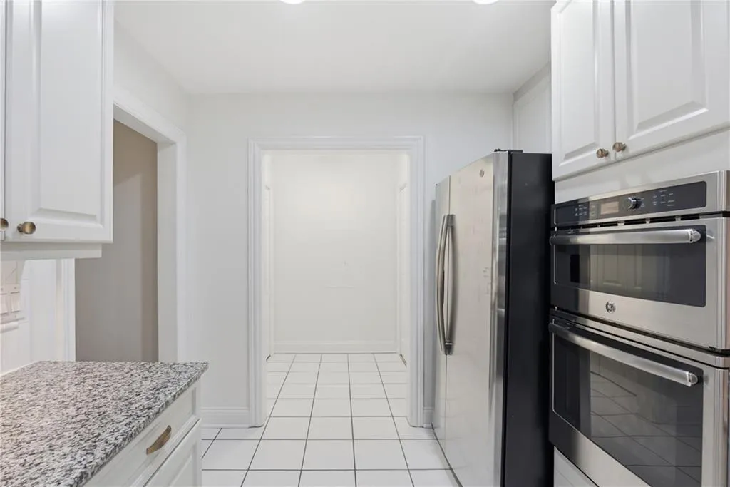 Kitchen featuring white cabinetry, granite countertops, stainless steel appliances, and tile flooring