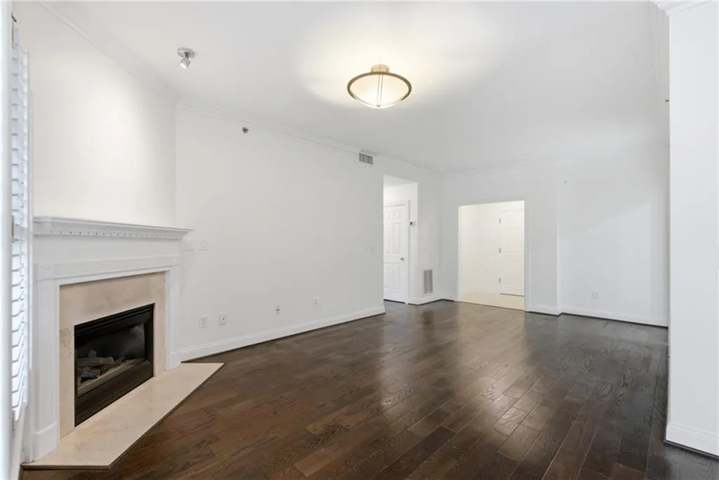 Living area featuring a fireplace with a light-toned surround and hearth, dark wood-finish flooring, white walls, crown molding, and a flush-mount ceiling fixture