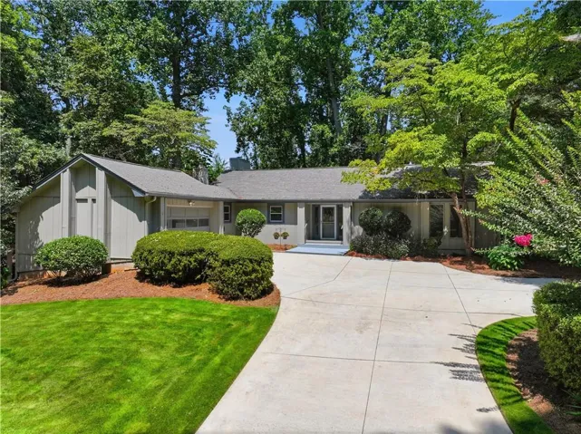 Single-story residence featuring a concrete driveway, mature trees, and manicured shrubs