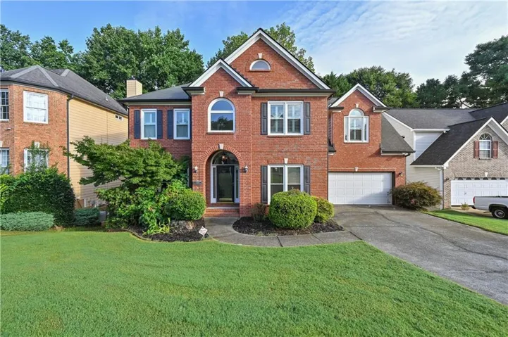 Brick exterior with multiple gables, arched entry, two-car garage, and landscaped front yard