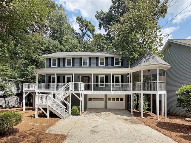 Two-story exterior with gray siding, a full-width covered porch, a screened turret porch, a two-car garage, and a concrete driveway