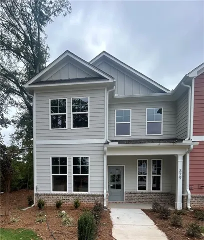 Two-story exterior with light gray siding, brick accents, covered front entry, multiple windowpanes, and a paved walkway