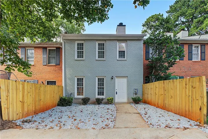 Brick exterior with painted finish, white entry door, four white-framed windows, and a wood privacy fence