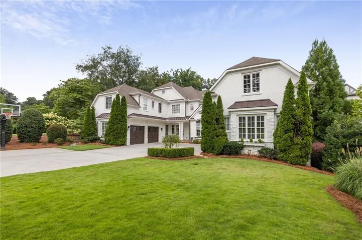 White brick exterior with a multi-gabled roof, two-car garage, concrete driveway, and mature landscaping