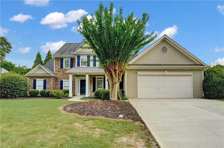 Two-story residence featuring a brick facade, blue window shutters, a covered entry porch with columns, an attached garage with a white door, and a concrete driveway