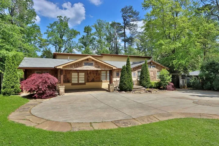 Stone facade with wood-wrapped columns, a circular driveway, and mature landscaping
