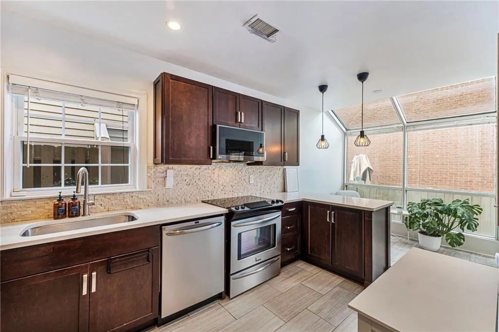 Kitchen featuring dark wood finish cabinets, stainless steel appliances, a peninsula, hanging light fixtures, and tasteful backsplash