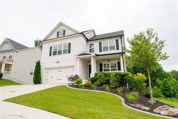Two-story residence featuring white brick and siding exterior, black shutters, a two-car garage, and a covered entry