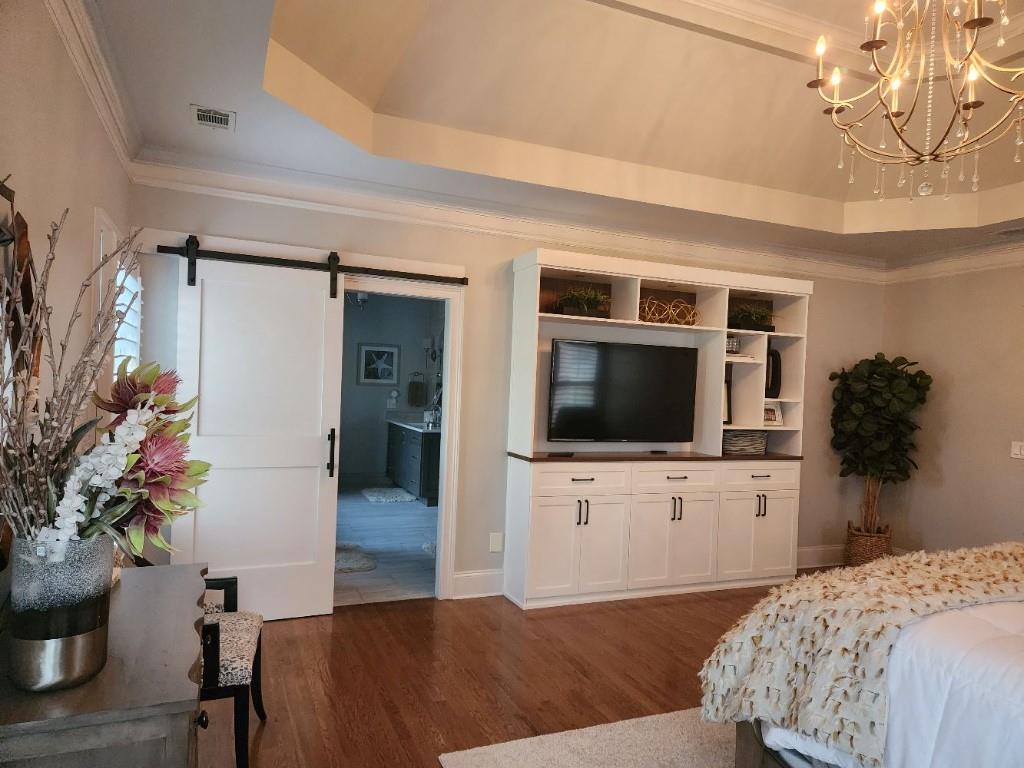 Bedroom featuring crown molding, a barn door, a chandelier, dark wood-type flooring, and a raised ceiling