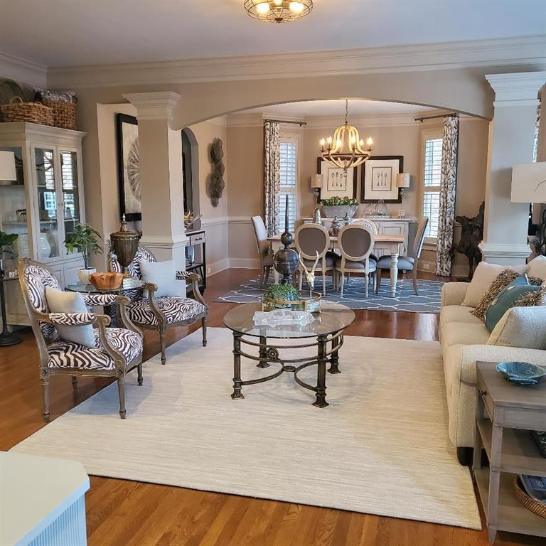 Living room featuring wood-type flooring, a chandelier, decorative columns, and crown molding