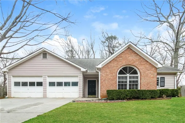 Brick and siding exterior featuring a prominent arched window and a two-car garage