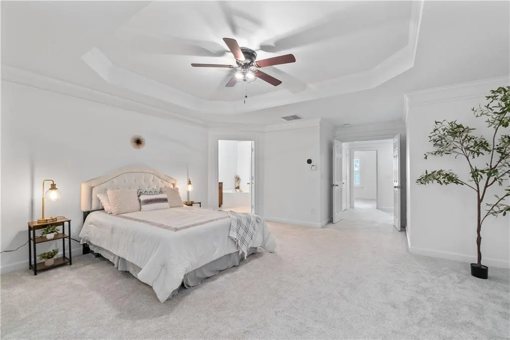 Bedroom with light colored carpet, crown molding, a raised ceiling, and ceiling fan