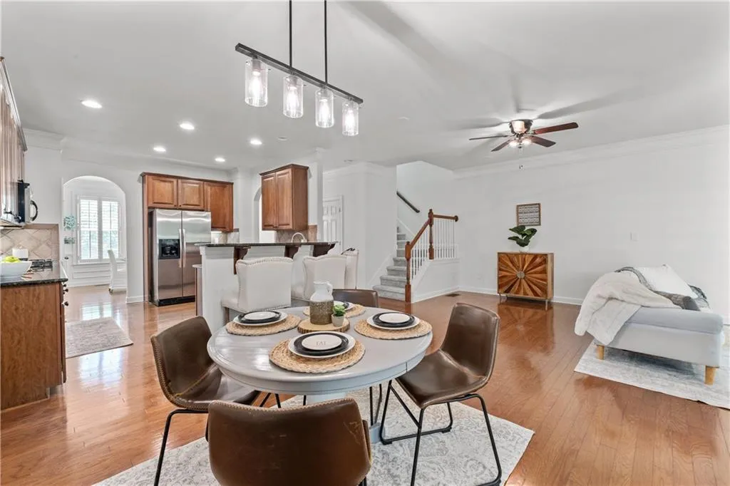 Dining room with arched walkways, ceiling fan, light wood finished floors, crown molding, and stairs