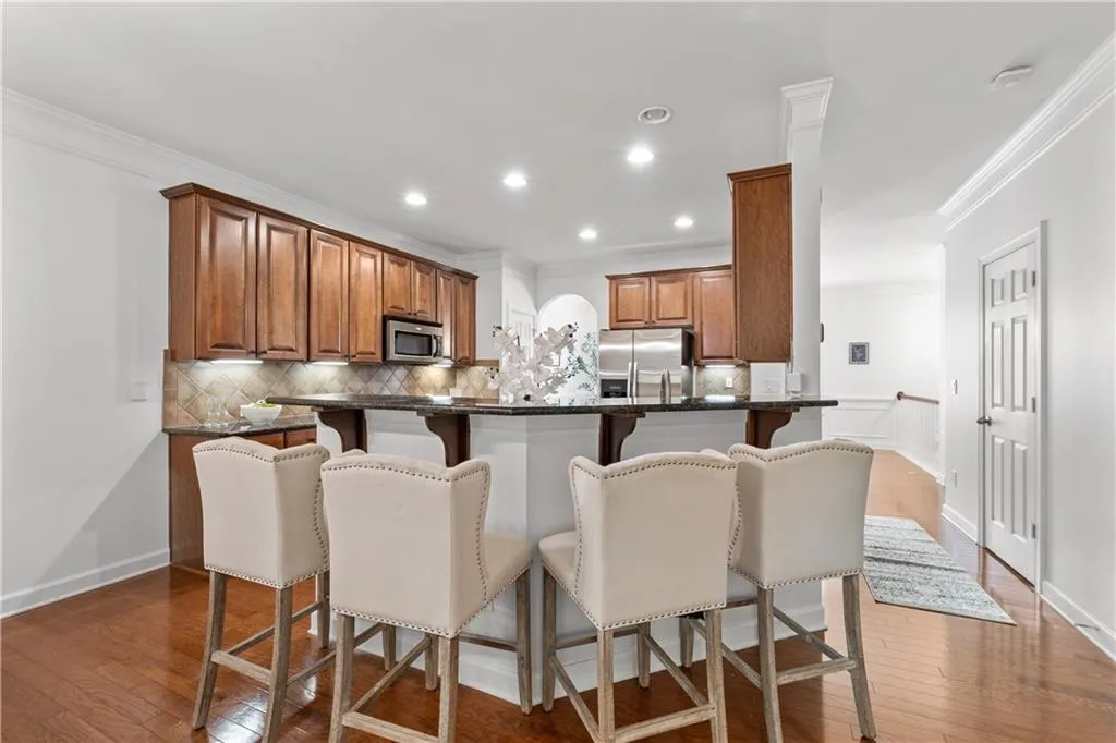 Kitchen featuring ornamental molding, a breakfast bar, hardwood / wood-style flooring, brown cabinetry, and tasteful backsplash