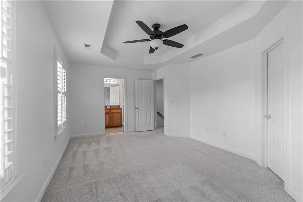 Unfurnished bedroom with a tray ceiling, light colored carpet, connected bathroom, and a ceiling fan