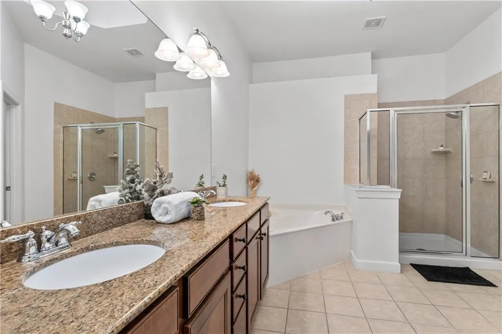 Bathroom with a chandelier, double vanity, a bath, a shower stall, and tile patterned floors