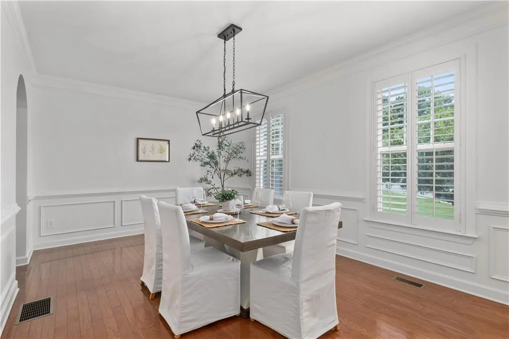 Dining room with crown molding, a decorative wall, arched walkways, a chandelier, and dark wood-style flooring